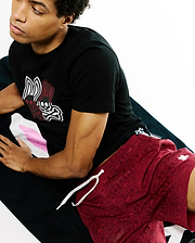 Black jersey t-shirt with large white/red Psycho Bunny skull logo, and deep red Mens Samos Hydrochromic Printed Swim Trunk with all-over bunny skull pattern, white drawstring, and small embroidered logo.