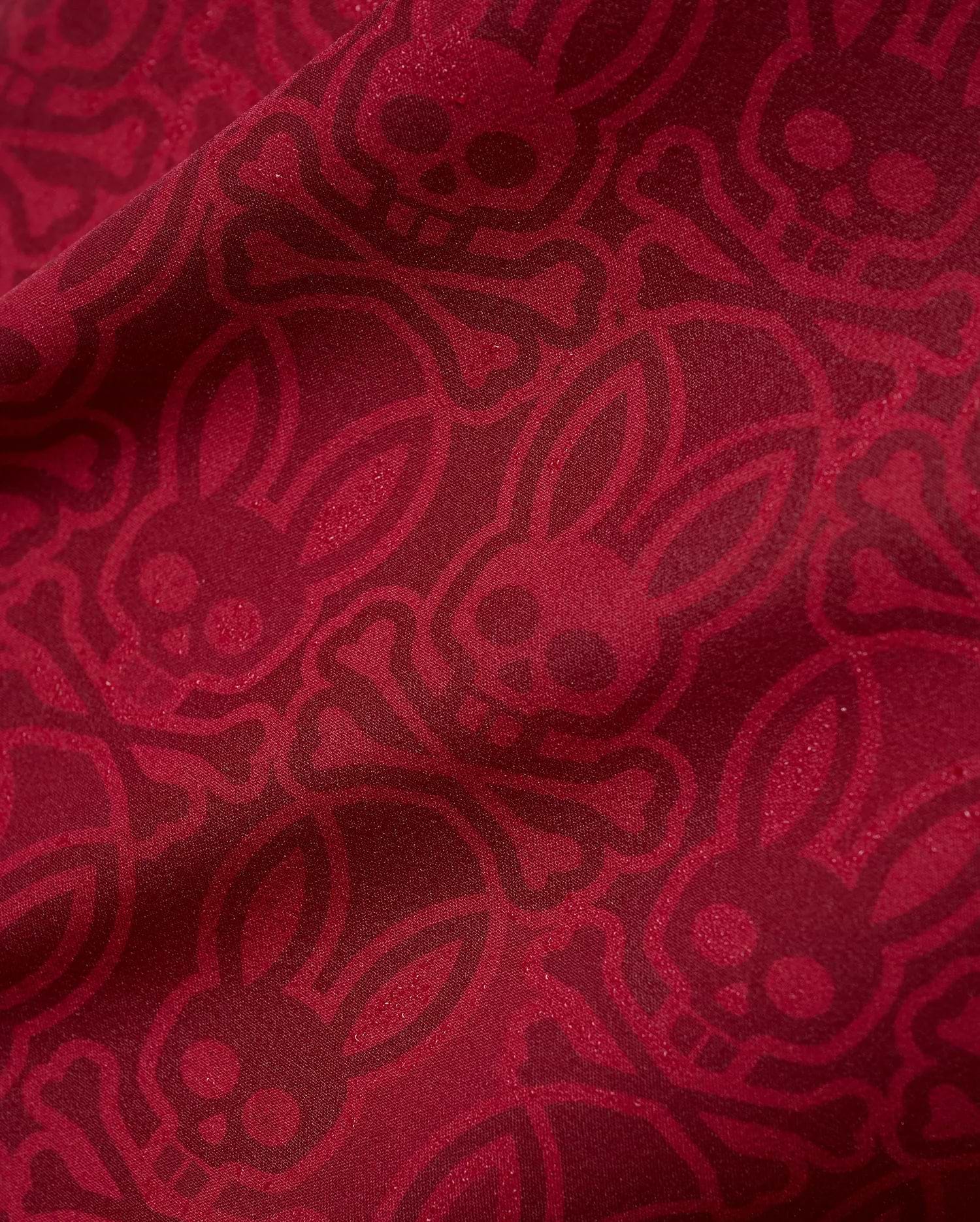 Mens Samos Hydrochromic Printed Swim Trunk in rich red, featuring an all-over darker red hydrochromic Psycho Bunny skull and crossbones pattern on smooth fabric.