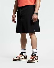 A person in coral quick-dry t-shirt, white socks, brown and white sneakers, and black Psycho Bunny MENS BIG AND TALL SAMOS HYDROCHROMIC SWIM TRUNK (B9W453F200) stands facing sideways with a watch on their relaxed left wrist.