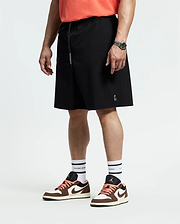 A person in coral quick-dry t-shirt, white socks, brown and white sneakers, and black Psycho Bunny MENS BIG AND TALL SAMOS HYDROCHROMIC SWIM TRUNK (B9W453F200) stands facing sideways with a watch on their relaxed left wrist.