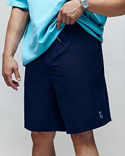 A person wearing Psycho Bunny’s MENS BIG AND TALL SAMOS HYDROCHROMIC SWIM TRUNK (B9W453F200), featuring a small embroidered logo near the hem, a mesh lining, and paired with a turquoise t-shirt and watch.