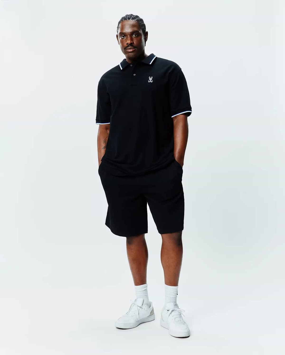 Black Big And Tall Sunny Pique Polo with white and light blue tipping on collar and cuffs, featuring a small embroidered Psycho Bunny skull logo on the left chest, paired with black shorts.