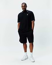Black Big And Tall Sunny Pique Polo with white and light blue tipping on collar and cuffs, featuring a small embroidered Psycho Bunny skull logo on the left chest, paired with black shorts.