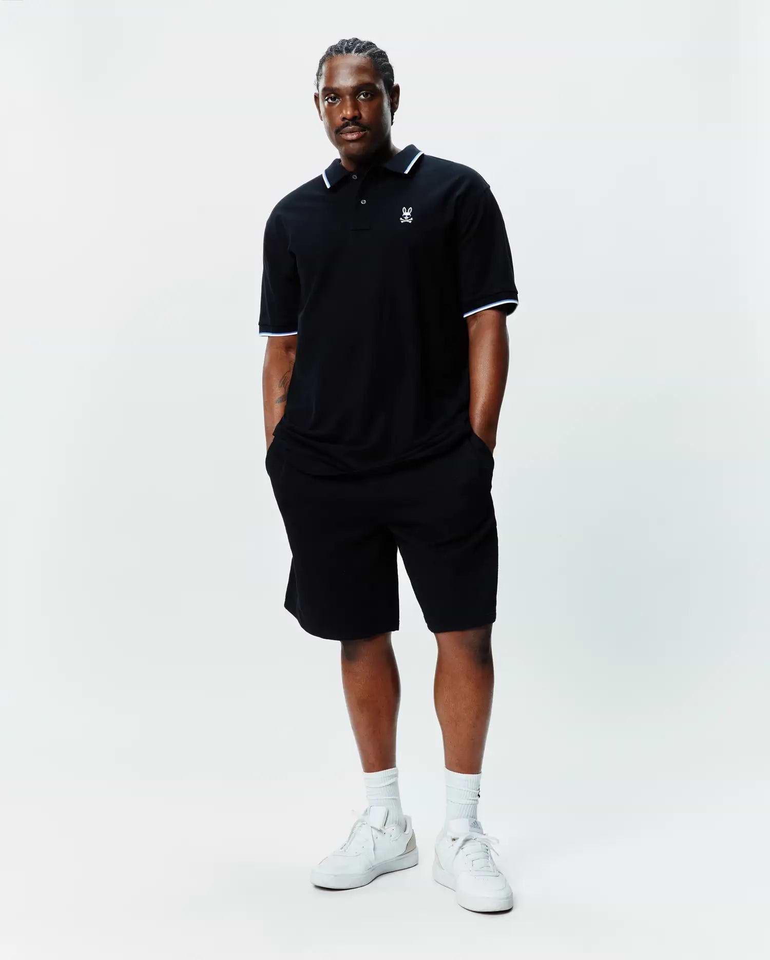 Black Big And Tall Sunny Pique Polo with white and light blue tipping on collar and cuffs, featuring a small embroidered Psycho Bunny skull logo on the left chest, paired with black shorts.