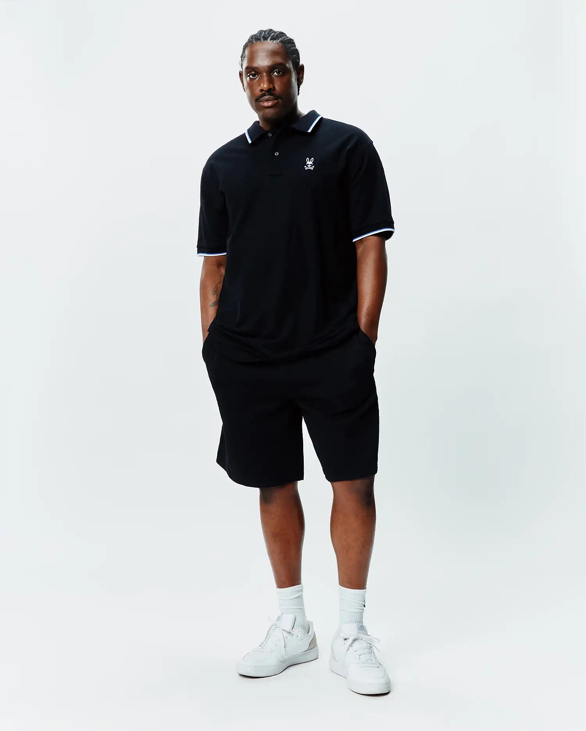 Black Big And Tall Sunny Pique Polo with white and light blue tipping on collar and cuffs, featuring a small embroidered Psycho Bunny skull logo on the left chest, paired with black shorts.