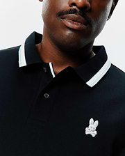 Black Mens Big And Tall Holden Pique Polo with a ribbed collar featuring white and light grey stripes, a two-button placket, and a small, embroidered Psycho Bunny skull logo on the left chest.