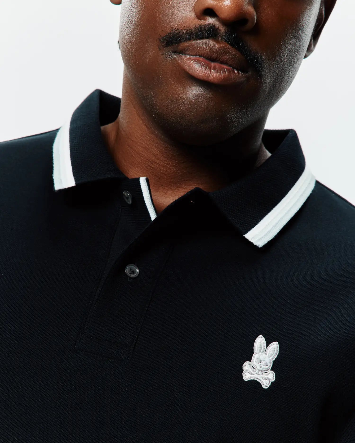 Black Mens Big And Tall Holden Pique Polo with a ribbed collar featuring white and light grey stripes, a two-button placket, and a small, embroidered Psycho Bunny skull logo on the left chest.