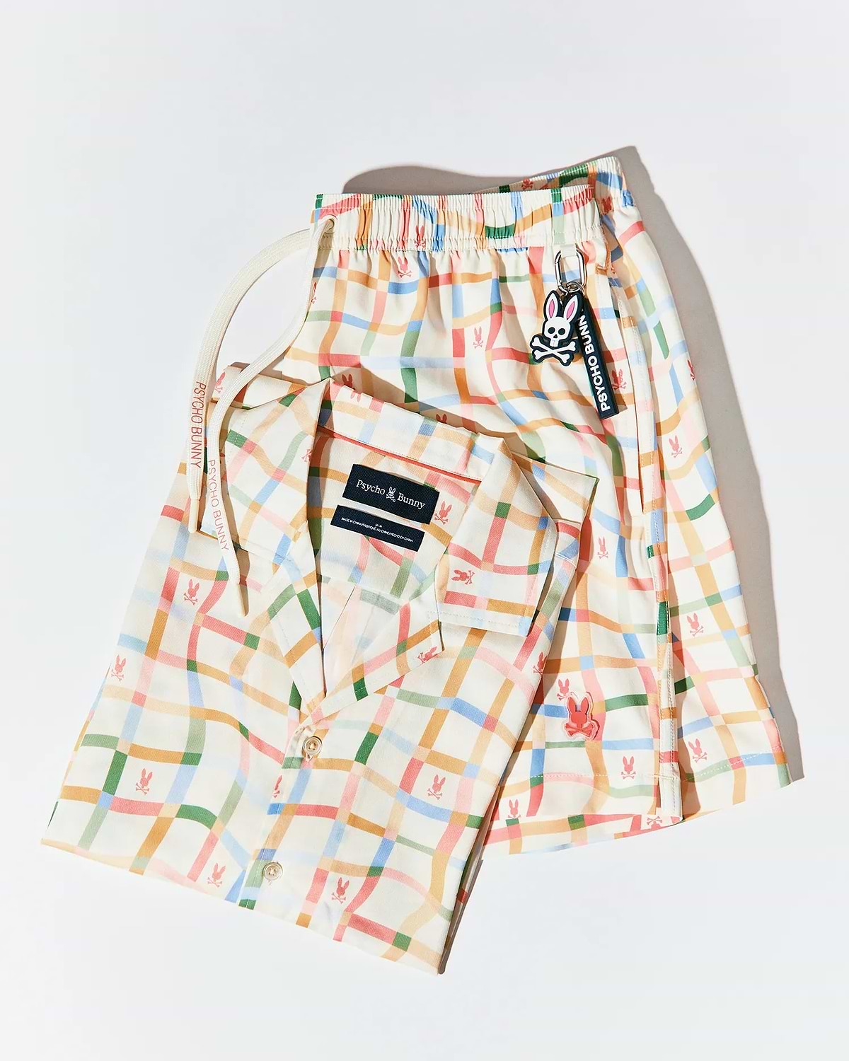 Mens Atlas Tencel Shirt and matching relaxed fit shorts in cream with a multicolor wavy plaid pattern featuring small repeated pink bunny skull logos, plus a Psycho Bunny drawstring and keychain.