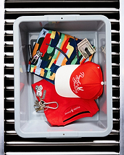 Red pique polo with chest Psycho Bunny logo, multi-color patterned swim shorts featuring bunny skull print and keychain, and a red and white Mens Sable A-Frame Trucker Cap with embroidered Psycho Bunny script.
