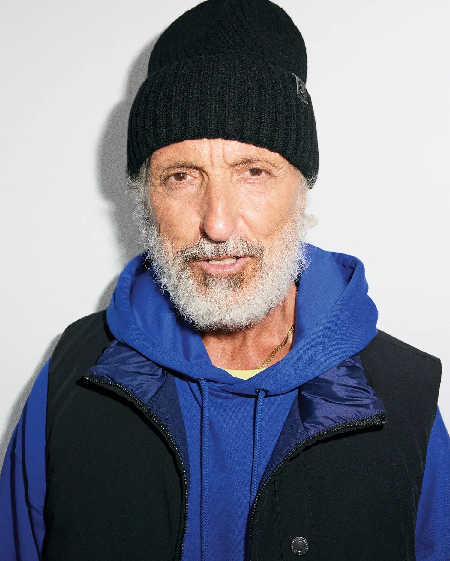 Black ribbed knit MENS BROGAN BEANIE with a subtle bunny skull logo patch, layered over a royal blue relaxed fit french terry hoodie and a black full-zip vest with a dark blue collar and branded snap button.
