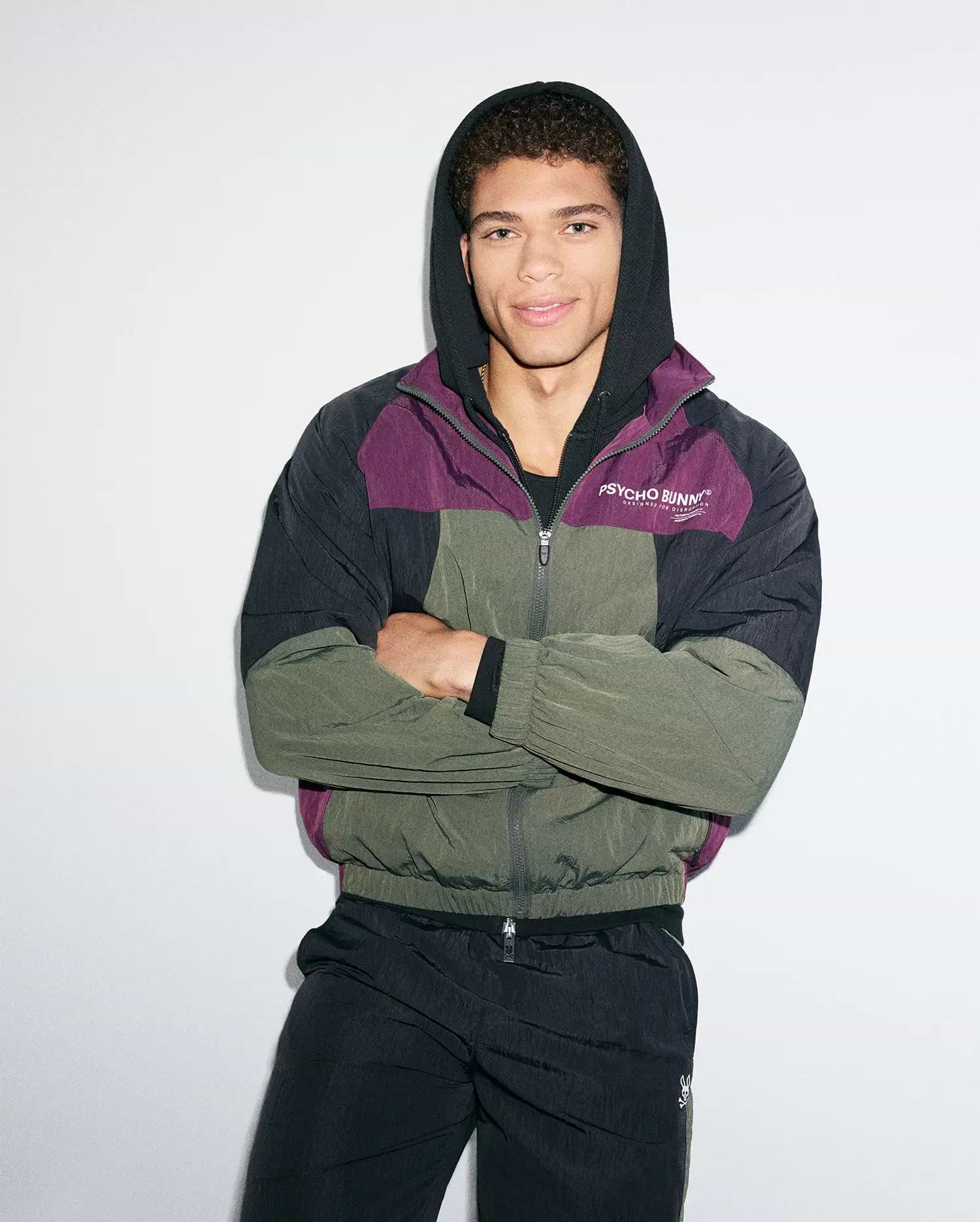 Mens Alder Nylon Colorblock Jacket, a relaxed fit, full-zip hooded jacket in crinkled nylon. Features black, deep purple, and olive green panels with a white Psycho Bunny chest logo and bunny skull zipper pull.