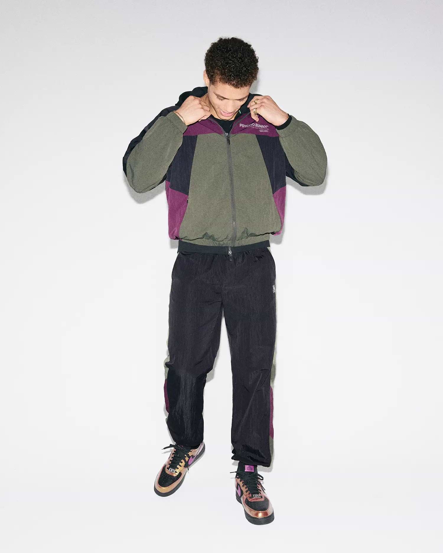 Olive, black, and purple colorblock crinkled nylon windbreaker jacket with Psycho Bunny chest text logo, paired with matching Mens Alder Nylon Colorblock Pant featuring side stripes and an embroidered bunny skull.