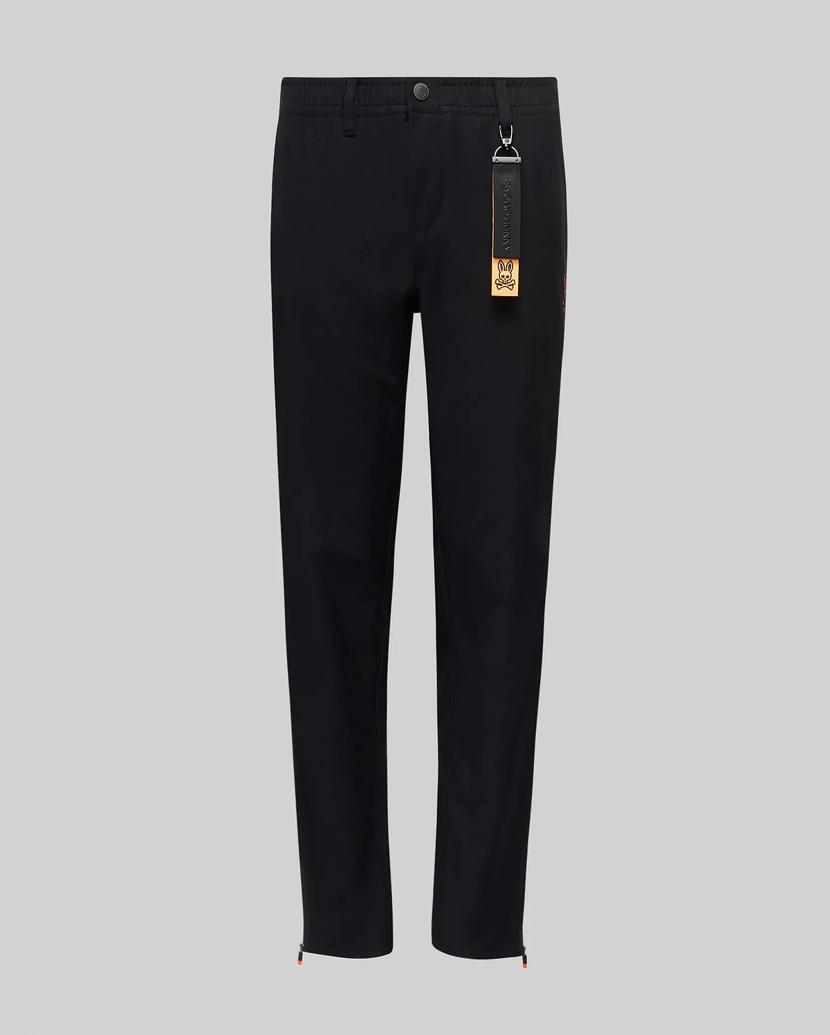 The Psycho Bunny KIDS MATHIEU COMMUTER PANT (KB0600002) features a black, straight-leg classic fit with a button and zip fly, elastic waistband, and a black tag with brown accent on the belt loop. Minimalist design shown on gray background.