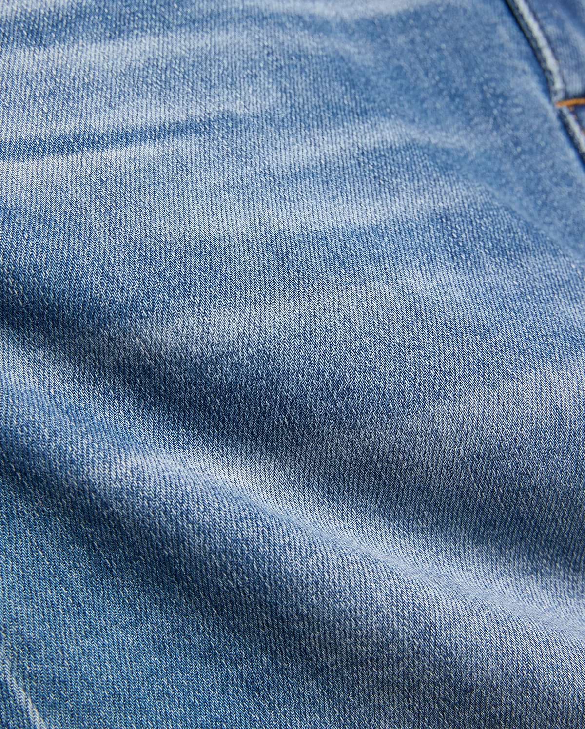 Kids Emerson Denim Pant featuring a classic medium blue washed denim with a prominent twill weave texture, natural fading, and subtle creasing, accented by visible warm brown stitching.