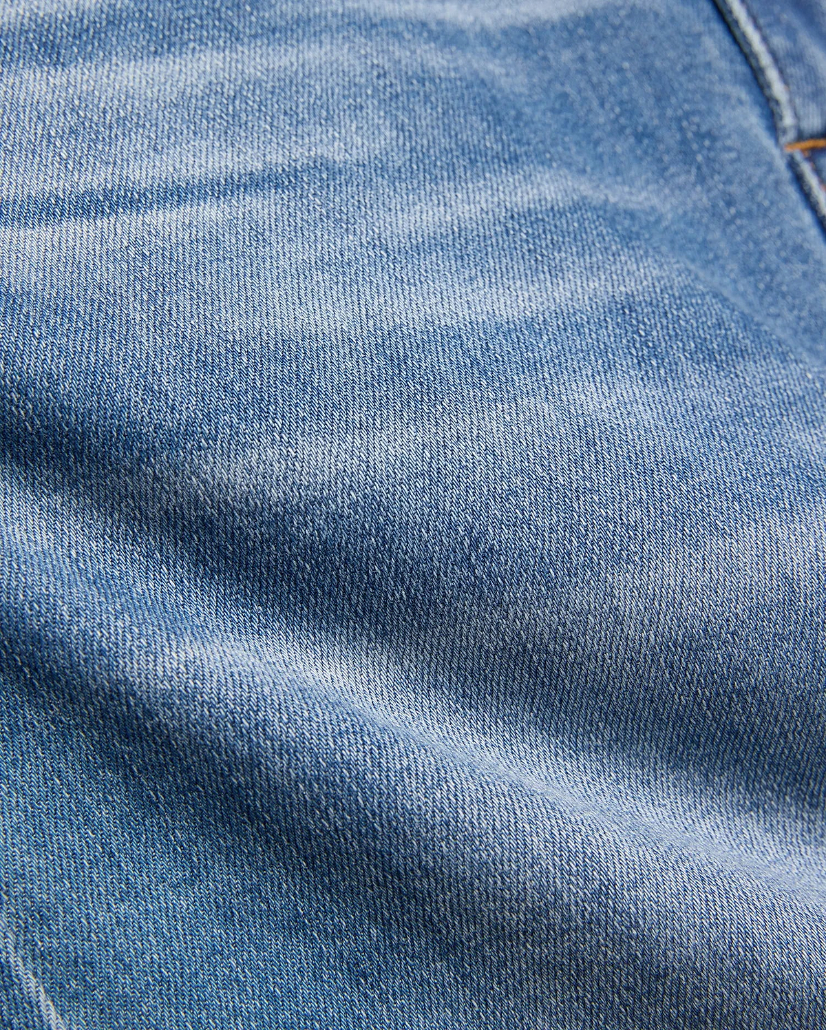 Kids Emerson Denim Pant featuring a classic medium blue washed denim with a prominent twill weave texture, natural fading, and subtle creasing, accented by visible warm brown stitching.