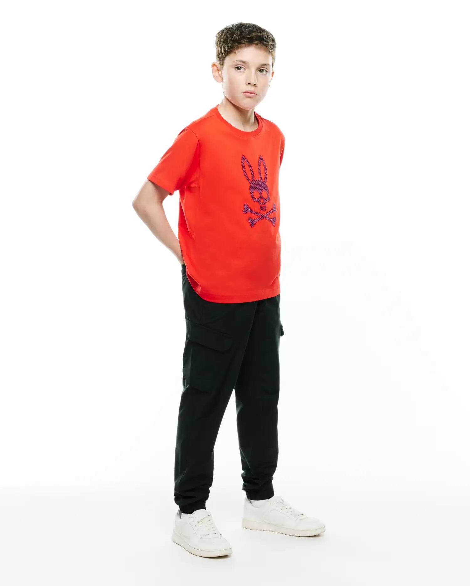 Orange jersey t-shirt with a large embroidered blue Psycho Bunny skull logo on the chest, paired with black Kids Luka Cargo Pant featuring side pockets and a relaxed jogger fit.