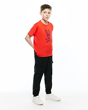 Orange jersey t-shirt with a large embroidered blue Psycho Bunny skull logo on the chest, paired with black Kids Luka Cargo Pant featuring side pockets and a relaxed jogger fit.