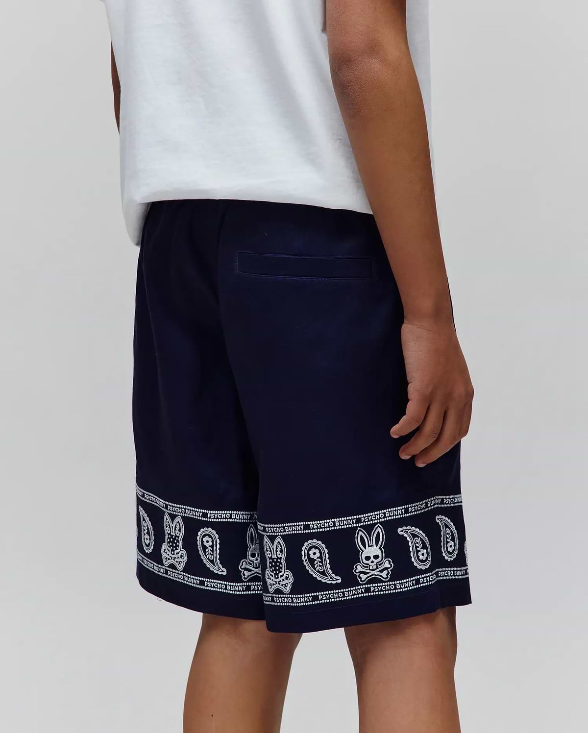 Kids Luke Tencel Short in navy, featuring a relaxed fit and a white bandana-style print along the hem with repeated Psycho Bunny skull logos and paisley patterns.