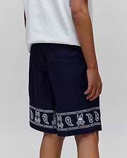 Kids Luke Tencel Short in navy, featuring a relaxed fit and a white bandana-style print along the hem with repeated Psycho Bunny skull logos and paisley patterns.