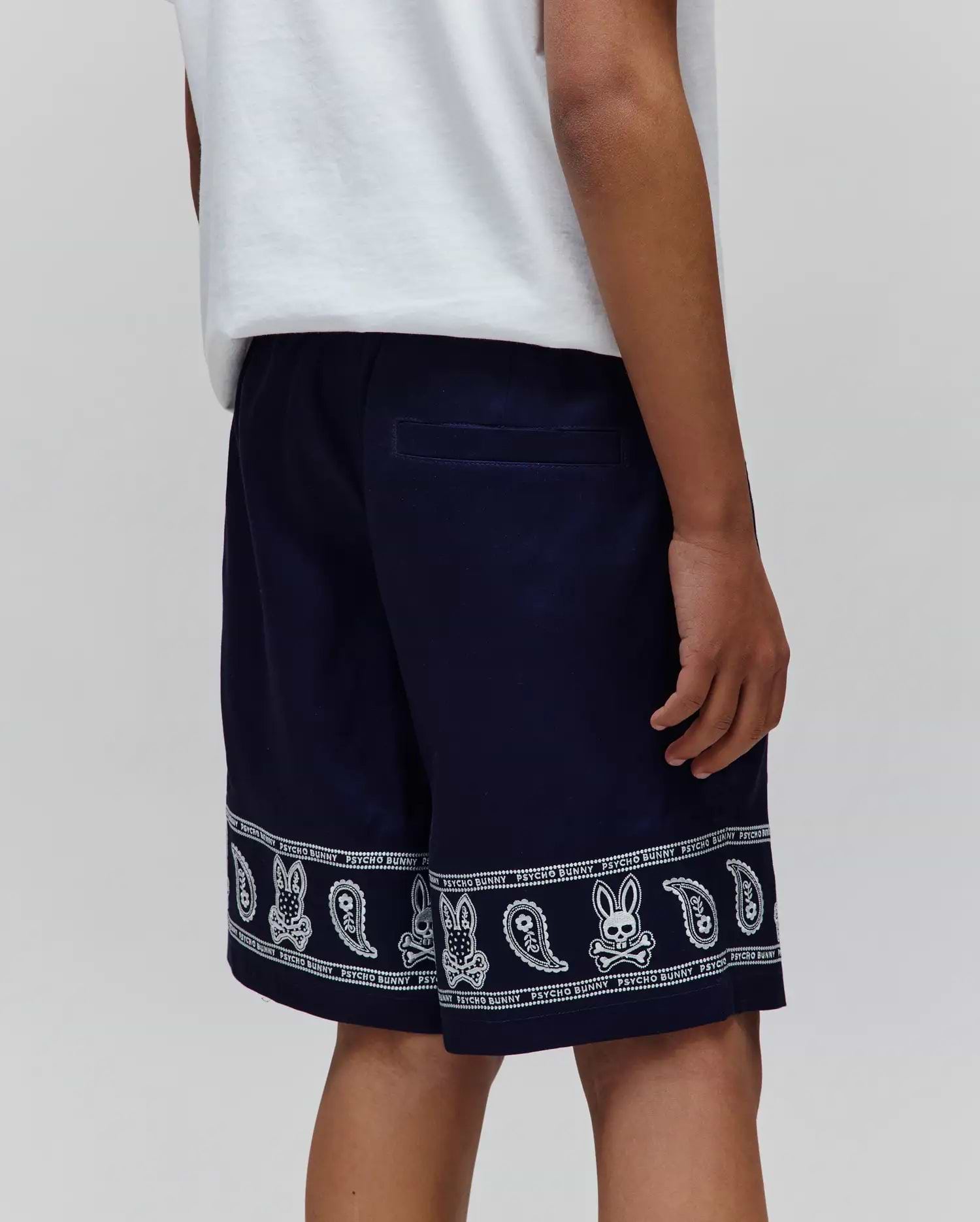 Kids Luke Tencel Short in navy, featuring a relaxed fit and a white bandana-style print along the hem with repeated Psycho Bunny skull logos and paisley patterns.