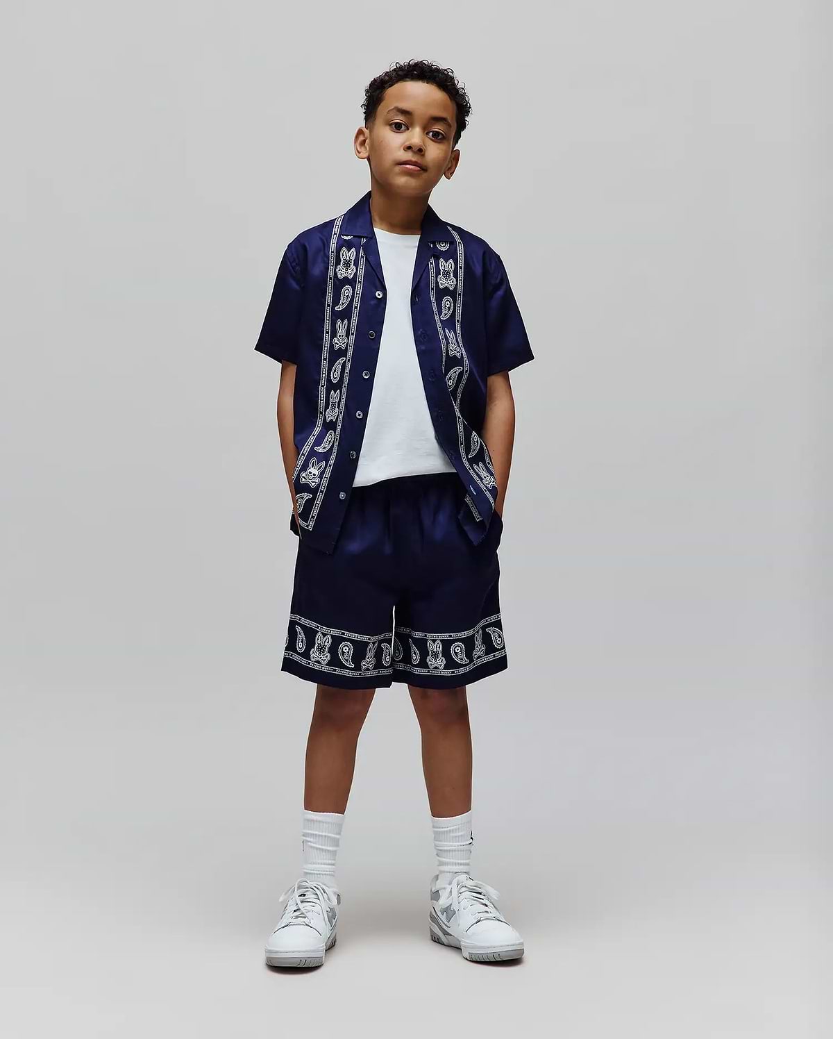 Navy blue Kids Luke Tencel Short and matching relaxed-fit short-sleeve button-up shirt, both featuring a white Psycho Bunny skull and paisley pattern with brand text along the shirt's placket and collar, and the shorts' hem.