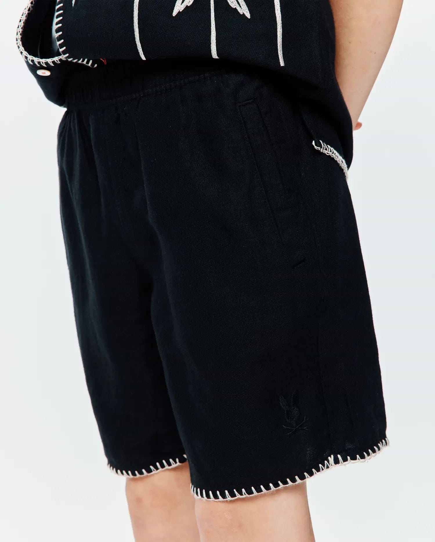 Kids Brad Linen Short in black, featuring a relaxed fit, textured linen fabric, white scalloped hem stitching, and a small tonal embroidered Psycho Bunny skull logo on the left leg.