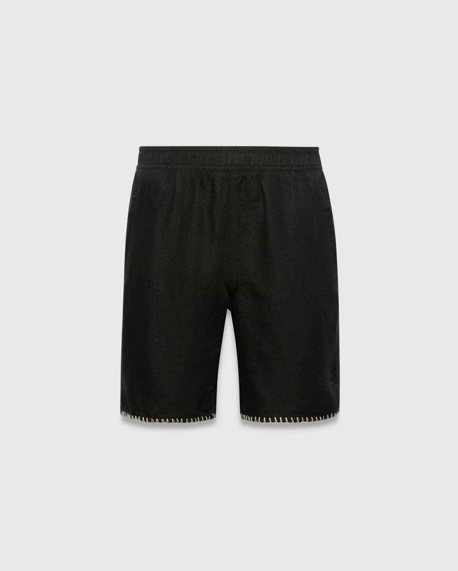 Kids Brad Linen Short, black relaxed fit with linen texture, featuring a subtle tonal embroidered Psycho Bunny skull logo on the lower right leg and white contrast blanket stitching on the hem.