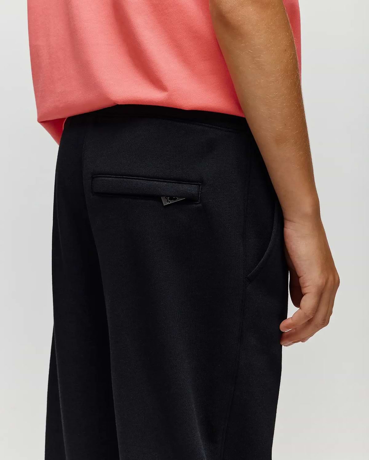 A person in Psycho Bunny KIDS WADE SWEATPANT - KB0800002 stands with their right arm relaxed, highlighting the back pocket and side seam details that showcase its classic athletic style.