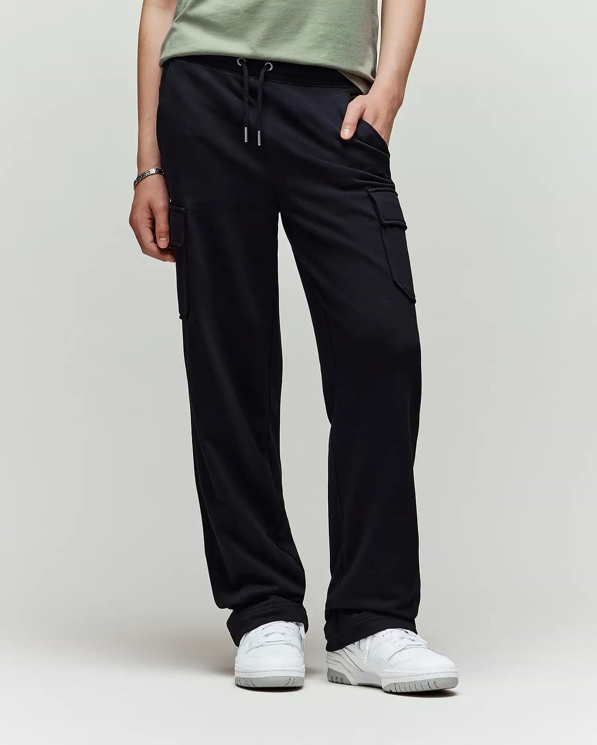 A child models Psycho Bunny’s KIDS NASH CARGO SWEATPANT - KB0800004 in green, showcasing utility cargo pockets and sweatpant comfort, with only the lower half and white sneakers visible against a plain light background.