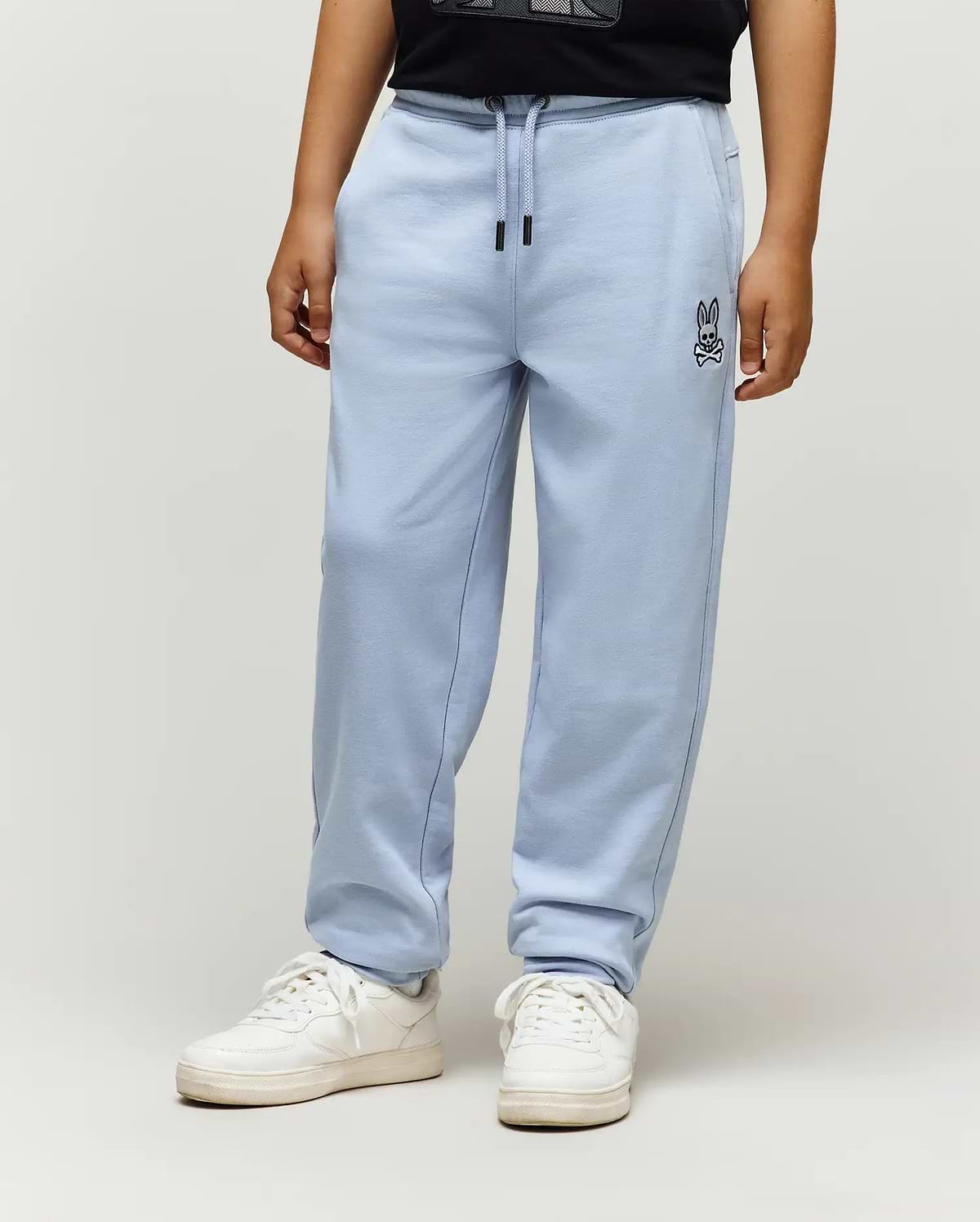 Kids Timothy 4K Bunny Jogger in light blue, a relaxed fit french terry jogger with an embroidered black Psycho Bunny skull logo on the left thigh and black drawstring tips.