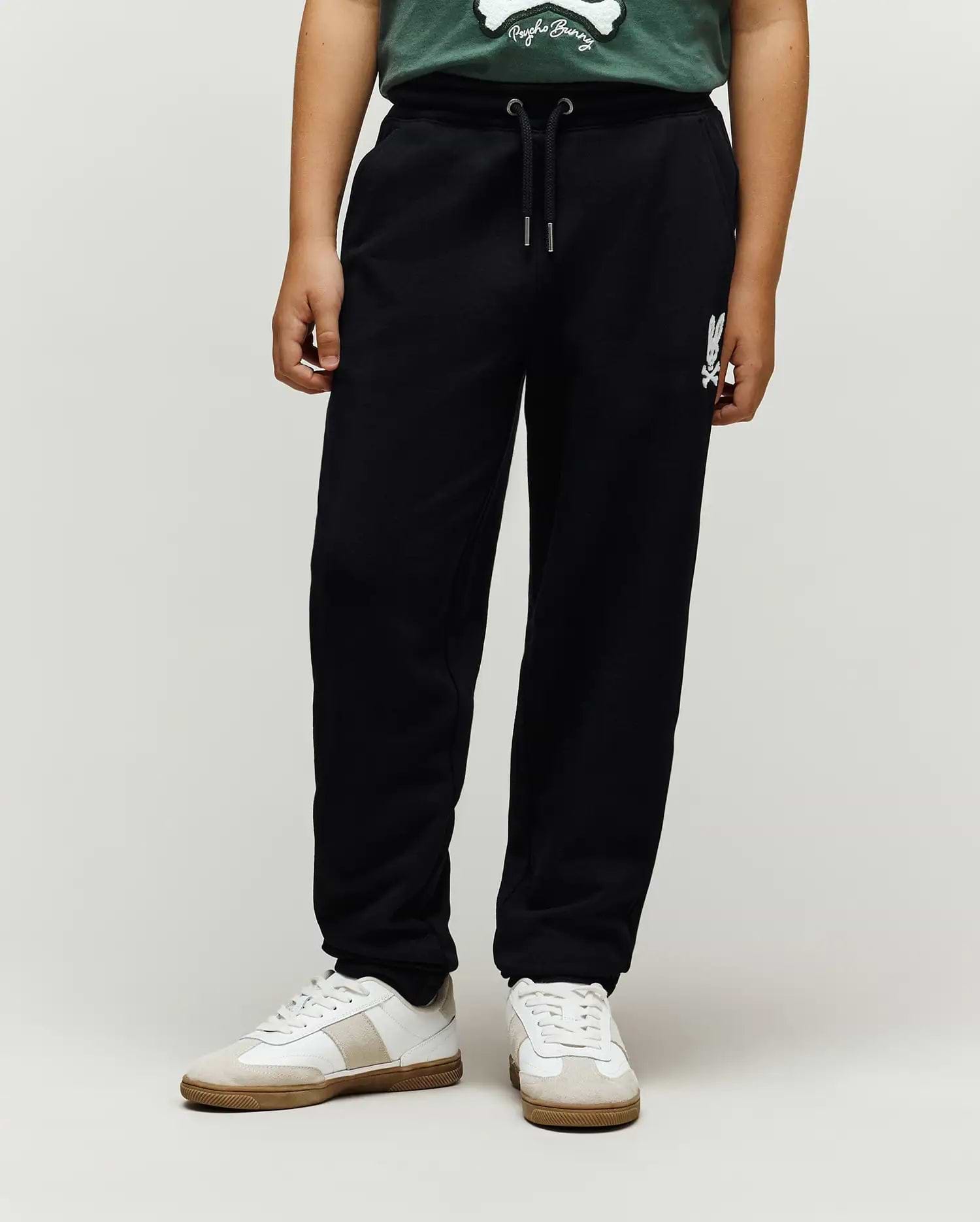 Kids Tate Chenille Sweatpant in black french terry, featuring a relaxed fit, drawstring waist, and a white chenille Psycho Bunny skull logo on the right thigh.