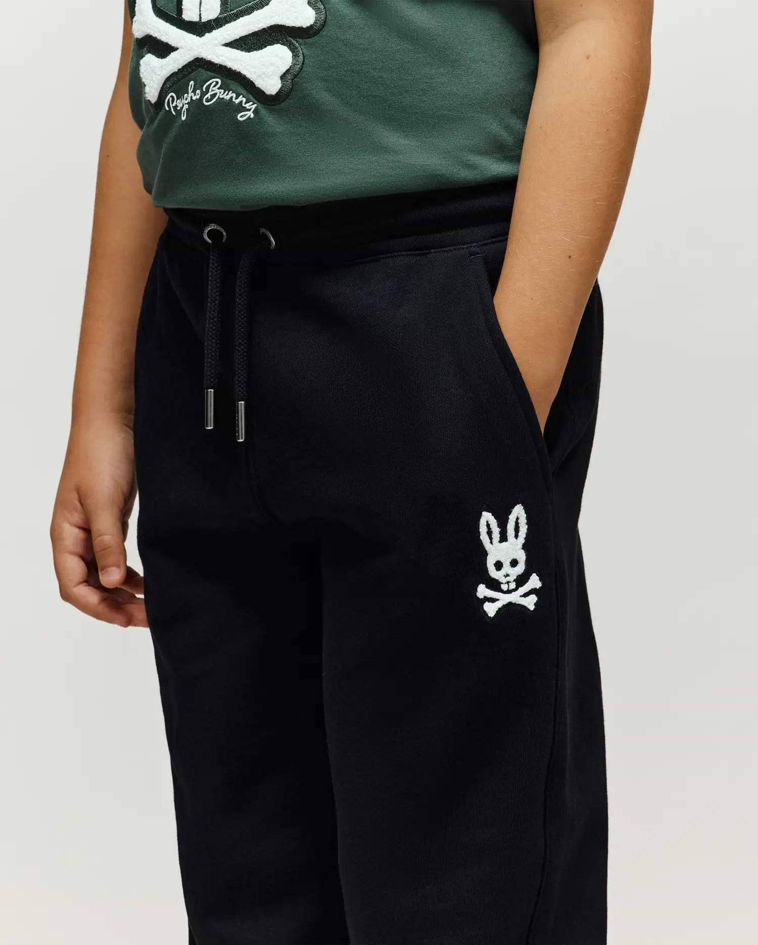 Kids Tate Chenille Sweatpant, black relaxed fit French terry sweatpants with drawstring waist, silver aglets, and a white chenille embroidered Psycho Bunny skull logo on left thigh.