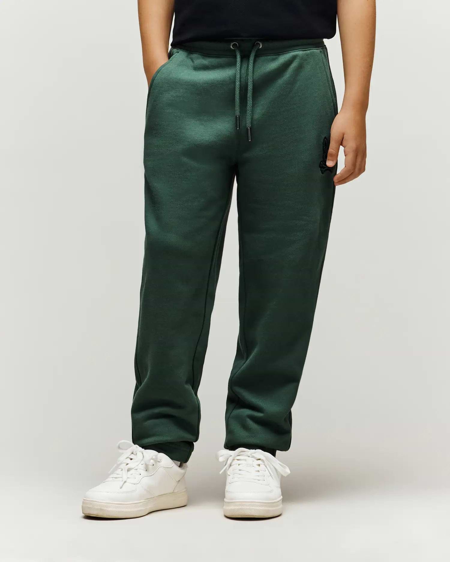 Kids Tate Chenille Sweatpant in dark green, a relaxed fit with drawstring waist, cuffed ankles, and a small embroidered black Psycho Bunny skull logo on the upper right thigh, featuring subtle ribbed side panels.