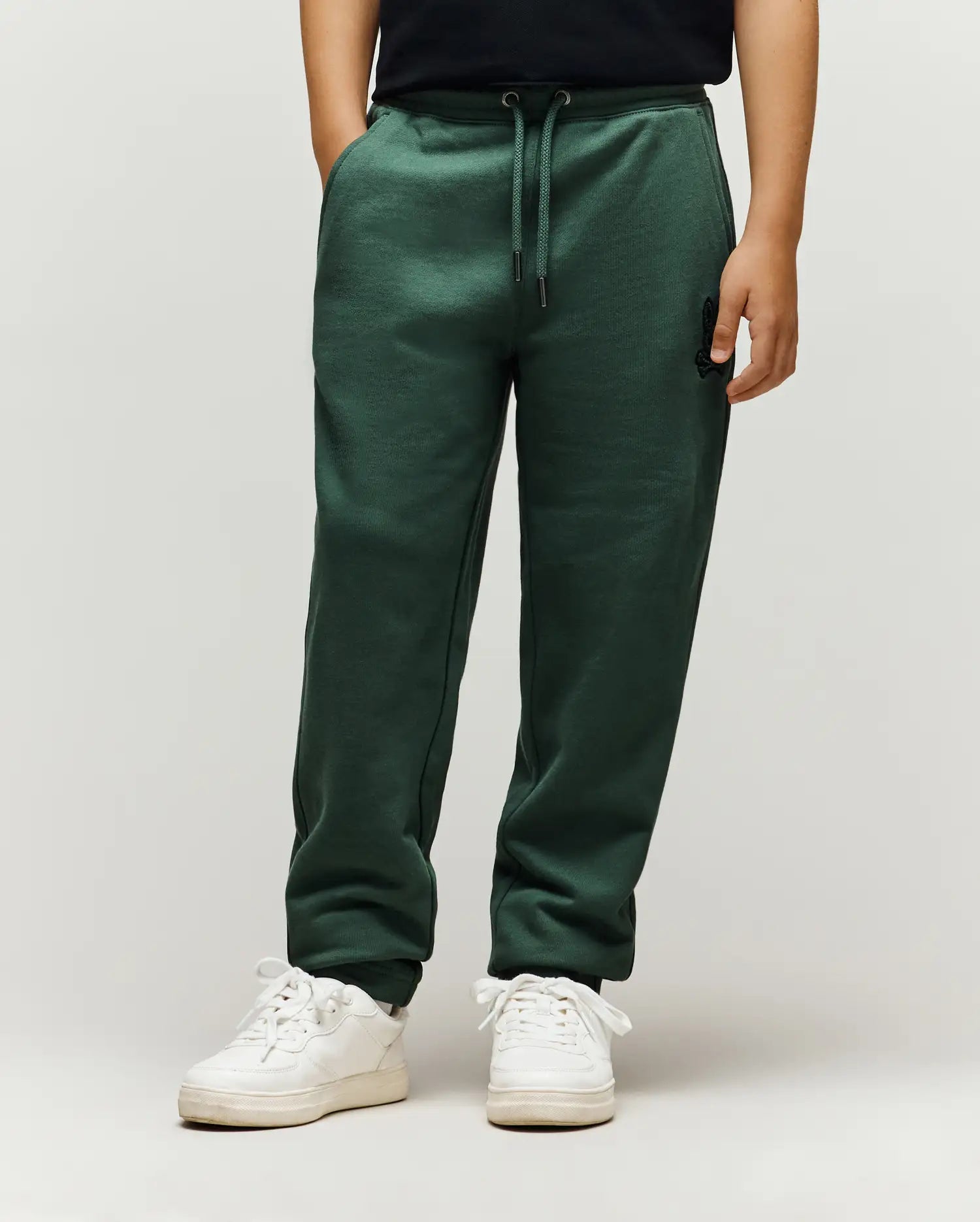 Kids Tate Chenille Sweatpant in dark green, a relaxed fit with drawstring waist, cuffed ankles, and a small embroidered black Psycho Bunny skull logo on the upper right thigh, featuring subtle ribbed side panels.