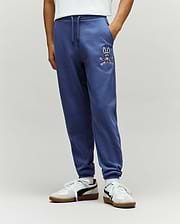 Kids Indigo Ski Bunny Sweatpant, a relaxed fit french terry jogger in deep blue, featuring a vibrant embroidered Psycho Bunny skull with goggles and crossed pink skis on the left thigh.