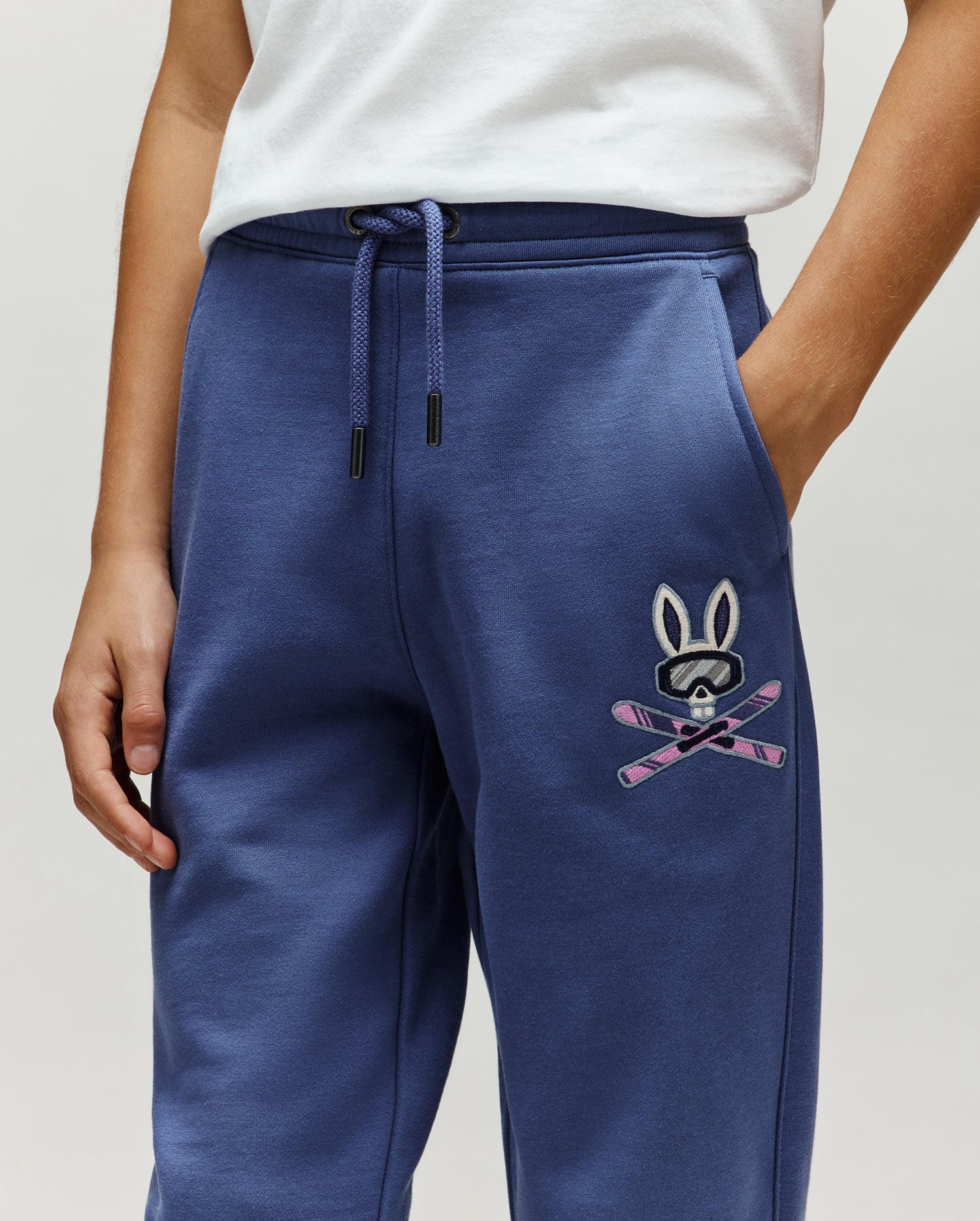 Kids Indigo Ski Bunny Sweatpant, relaxed fit, made from soft french terry, features a medium-sized embroidered Psycho Bunny skull with ski goggles and crossed pink skis on the left thigh.