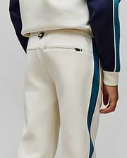 Kids Caspian Contrast Stripe Track Pant in cream french terry, featuring a relaxed fit, teal and white side stripes, a small Psycho Bunny logo tag on the waistband, and a zippered back pocket.