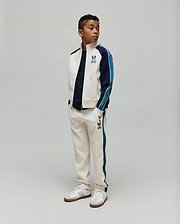 Cream track suit: jacket with navy/teal color block sleeves, chest Psycho Bunny skull logo; KIDS Caspian Contrast Stripe Track Pant with teal side stripes, thigh bunny skull logo. Classic fit.