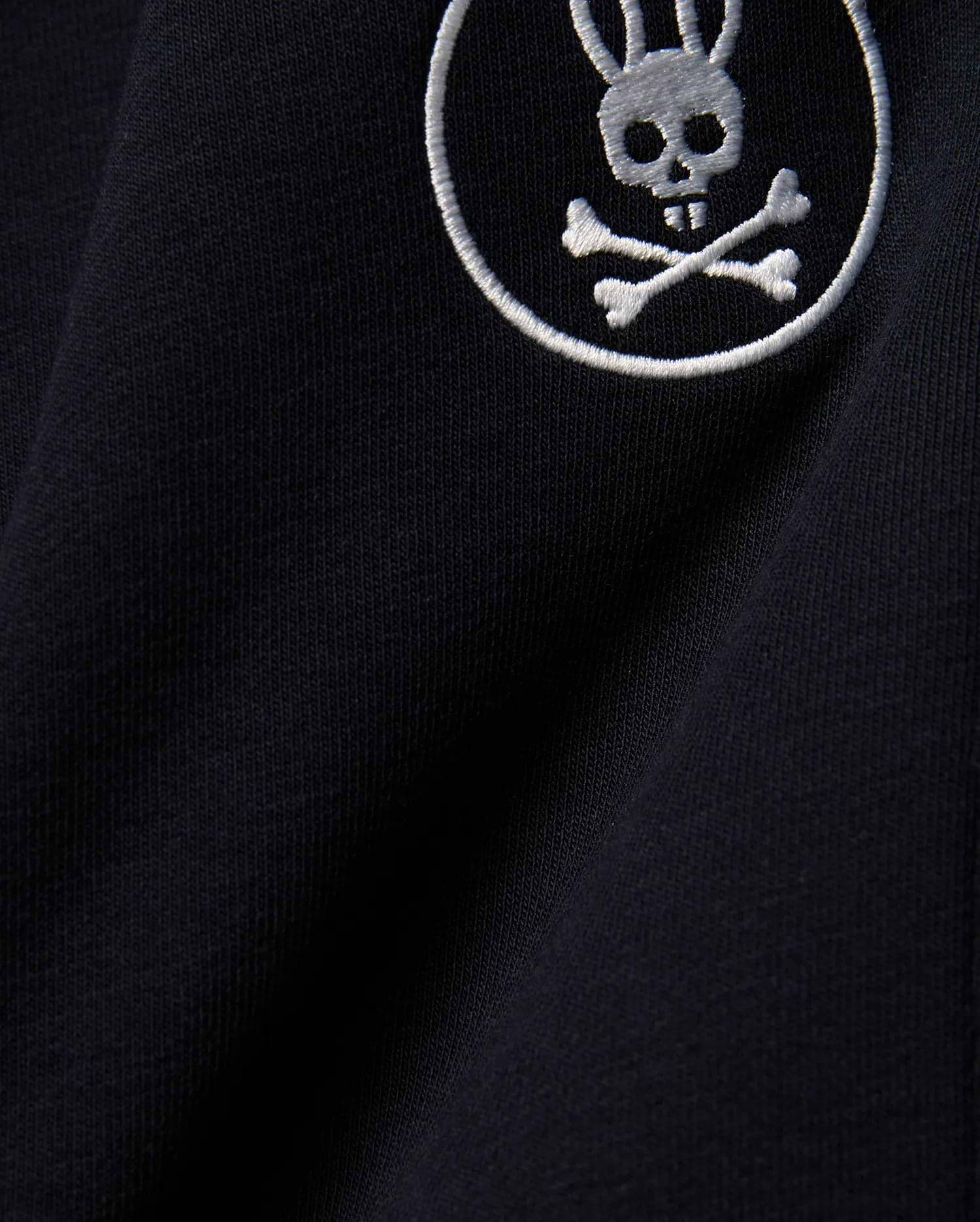 Kids Nathaniel Sweatpant in deep navy blue, crafted from soft jersey knit fabric, featuring a prominent white embroidered Psycho Bunny skull and crossbones logo.
