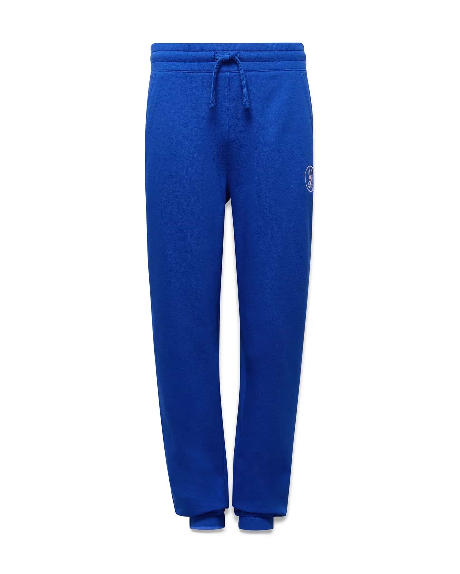 KIDS NATHANIEL SWEATPANT. Relaxed fit royal blue soft jersey sweatpants with a drawstring waist, ribbed cuffs, and a small embroidered light blue Psycho Bunny skull logo on the left thigh.