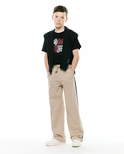 Black jersey t-shirt with a large white and red Psycho Bunny skull graphic, paired with a black French terry hoodie draped over shoulders and KIDS TY FRENCH TERRY SWEATPANT in beige with a dark side stripe and small embroidered logo.