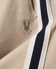 Kids Ty French Terry Sweatpant in beige french terry fabric, featuring a small embroidered Psycho Bunny skull logo and a navy and white side stripe.