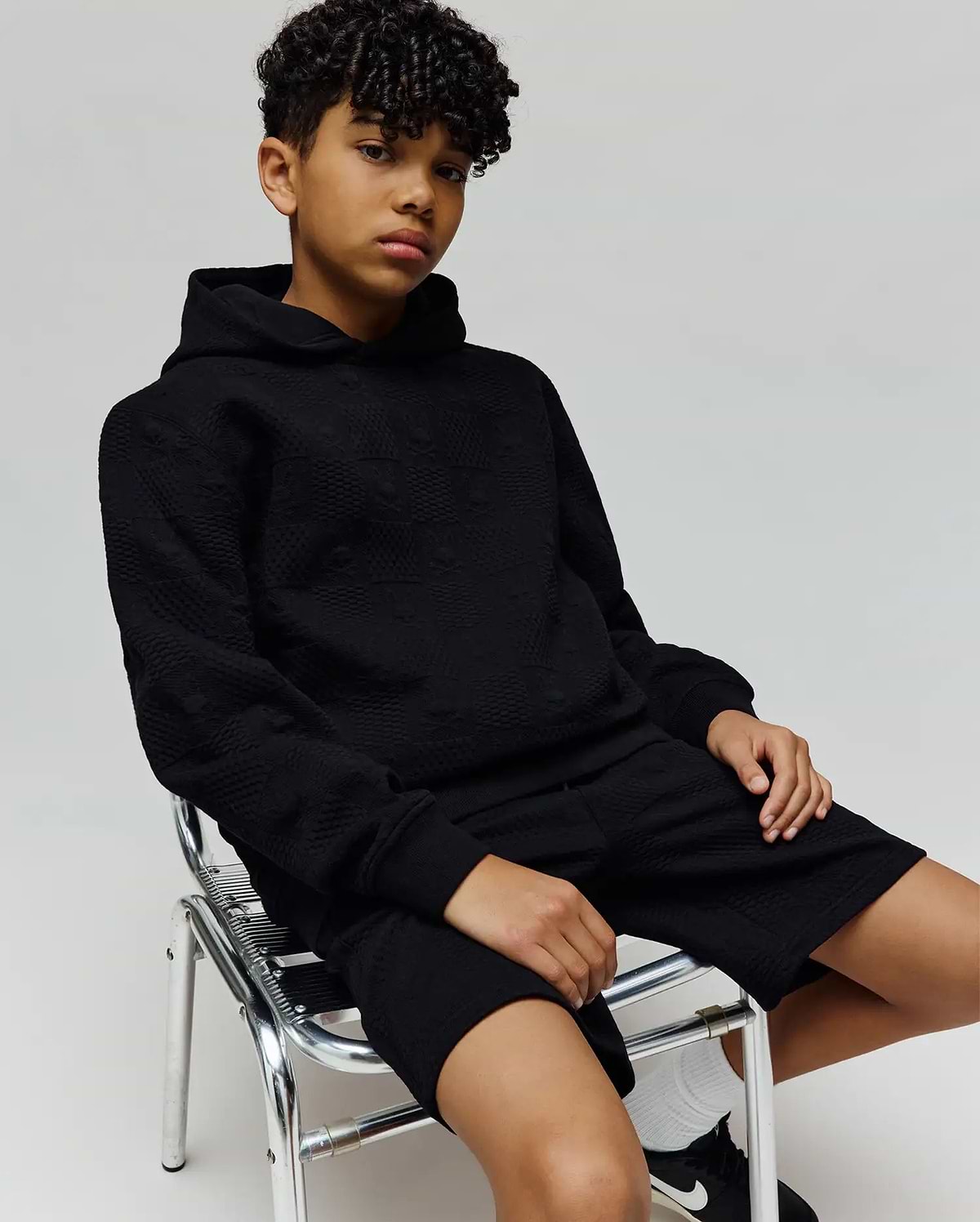 Black relaxed fit hoodie and Kids Dustin Sweatshort set, featuring an all-over subtle embossed Psycho Bunny skull logo pattern on textured knit fabric.