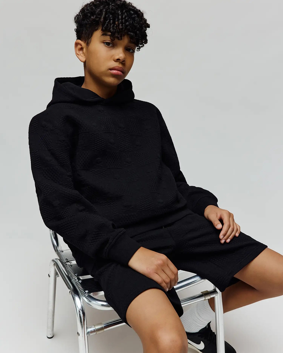 Black relaxed fit hoodie and Kids Dustin Sweatshort set, featuring an all-over subtle embossed Psycho Bunny skull logo pattern on textured knit fabric.