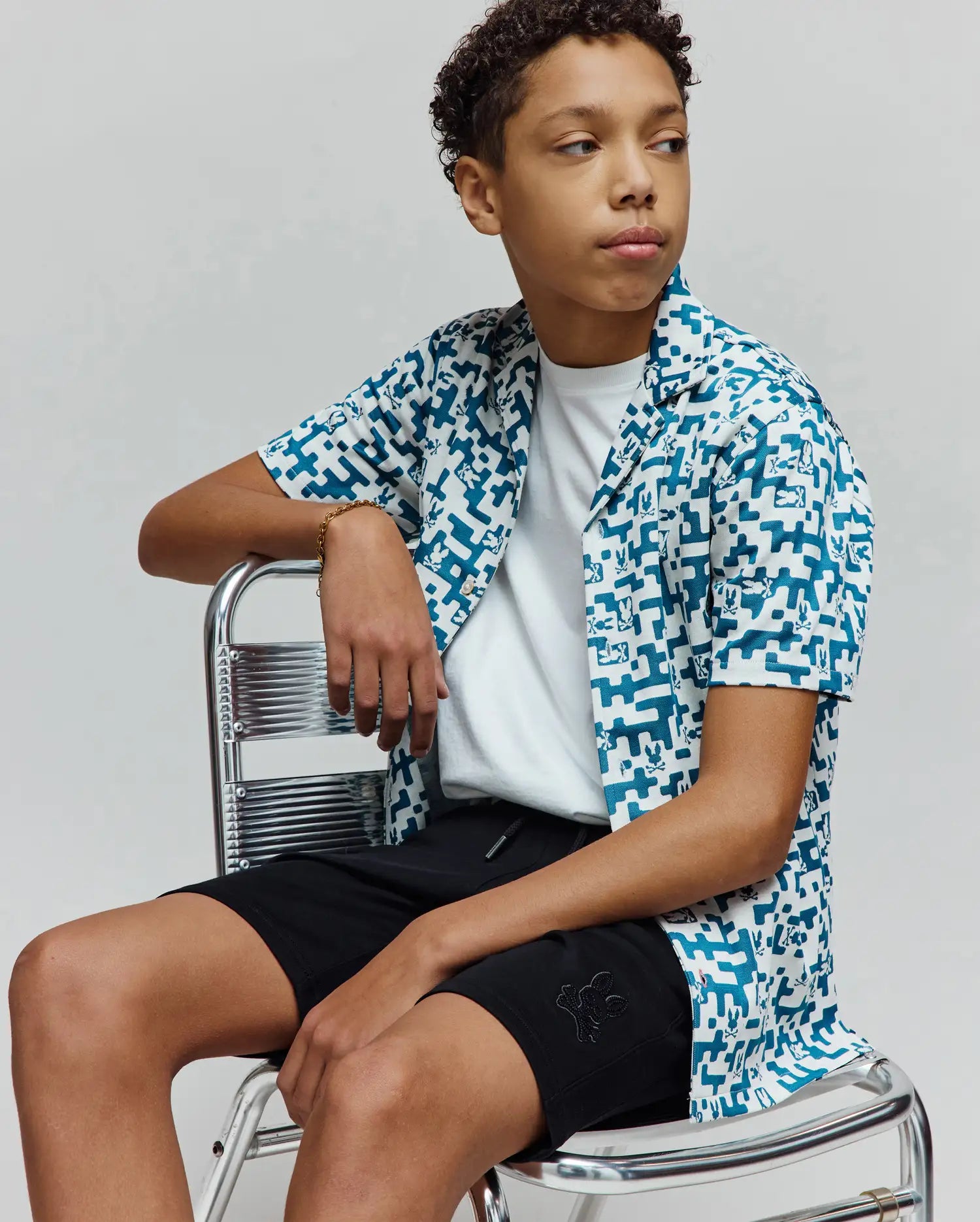 Relaxed fit white and teal pixelated Psycho Bunny logo print short-sleeve camp shirt, layered over a white jersey tee, with black Kids Barry Modal Short featuring an embroidered Psycho Bunny logo.