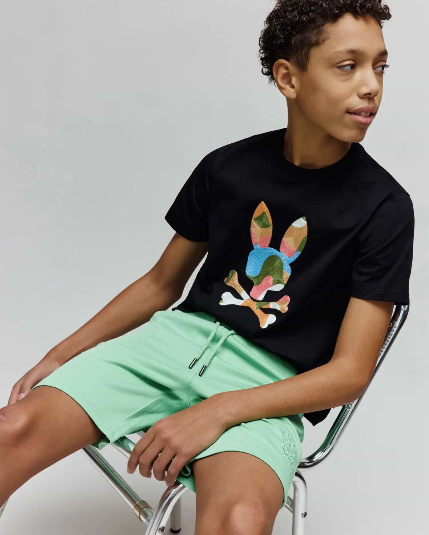 Black jersey t-shirt with a large multi-color camo Psycho Bunny skull graphic on the chest, paired with Kids Barry Modal Short in mint green featuring a drawstring waist and small tonal embroidered logo.