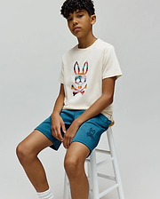 Cream jersey t-shirt with a large, colorful plaid Psycho Bunny skull graphic on the chest, paired with relaxed fit Teal KIDS BARRY MODAL SHORT featuring a small embroidered Psycho Bunny logo on the left leg.