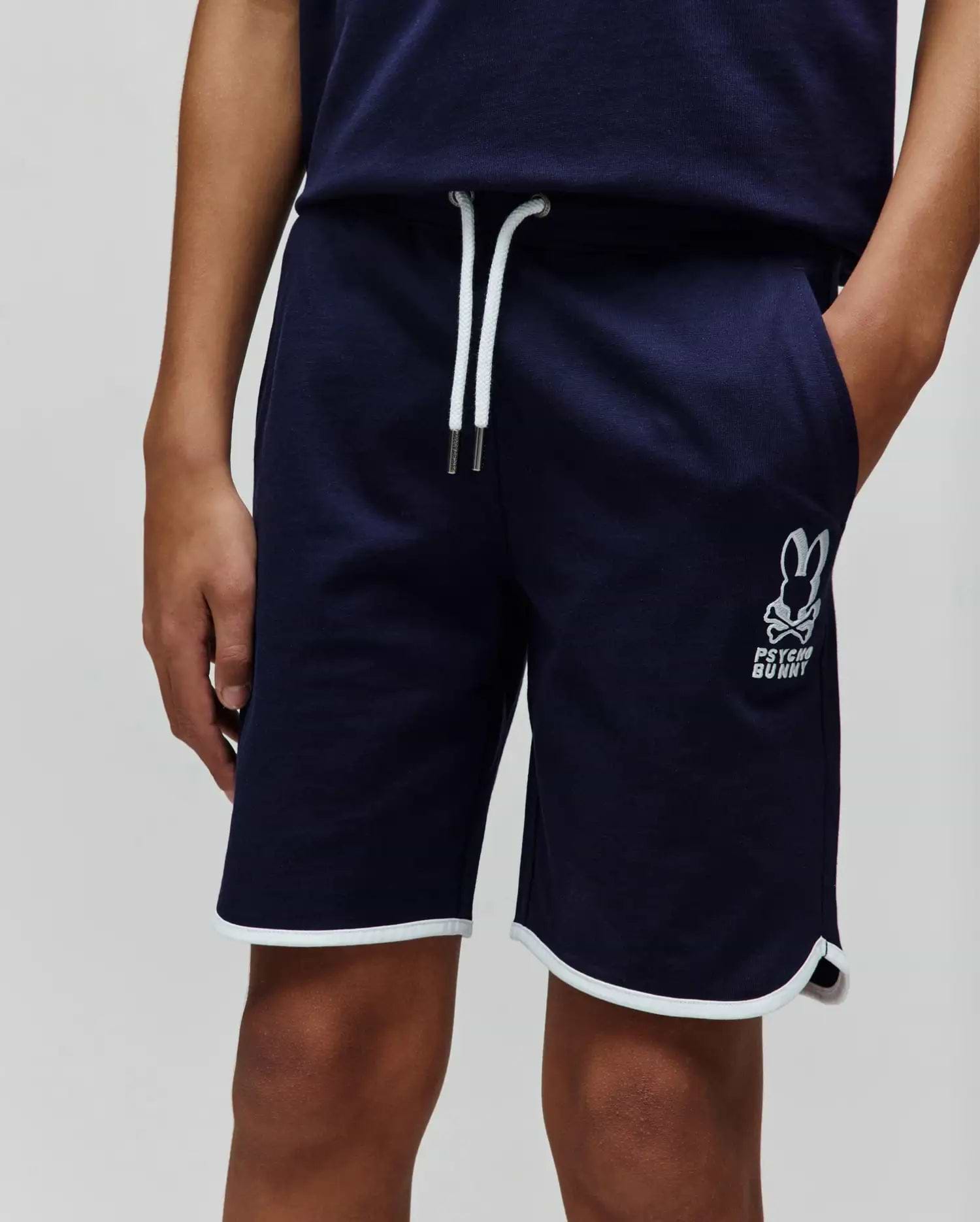 Kids Toby Short, navy French terry shorts with a relaxed fit, featuring white drawstrings, a large embroidered Psycho Bunny skull logo on the left leg, and white piping on the curved hem.