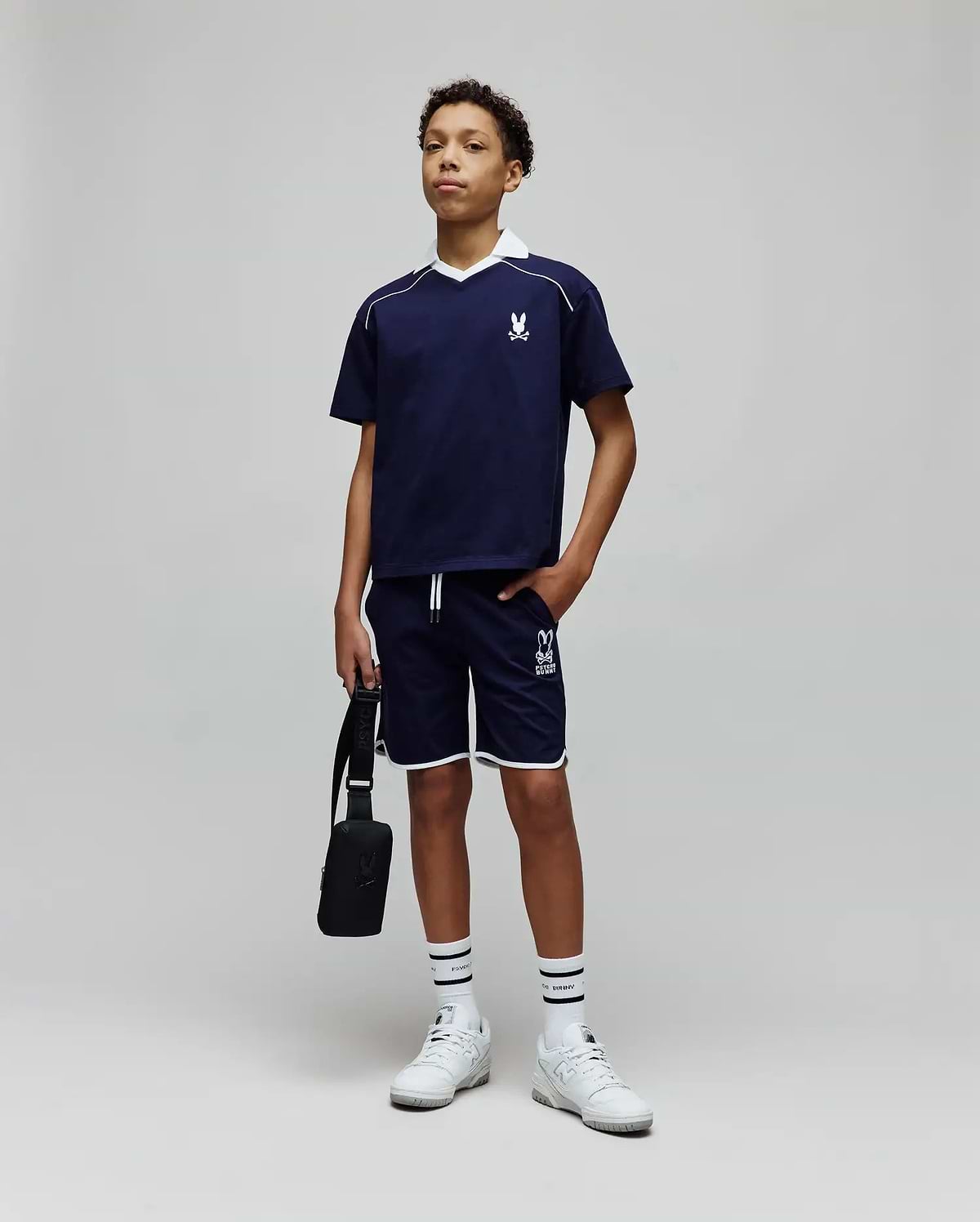 Navy blue polo with white collar and piping, featuring an embroidered bunny skull on the chest, and Kids Toby Short with white trim and a large Psycho Bunny text logo on the leg.
