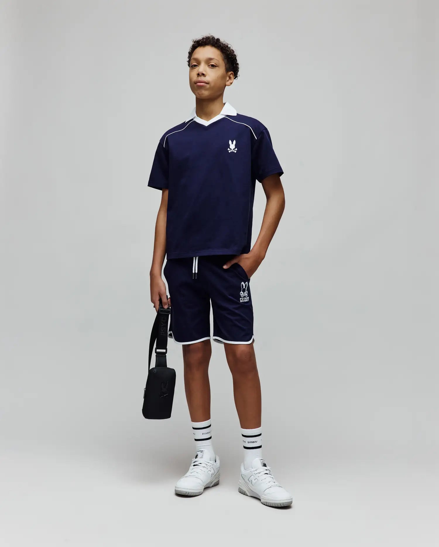 Navy blue polo with white collar and piping, featuring an embroidered bunny skull on the chest, and Kids Toby Short with white trim and a large Psycho Bunny text logo on the leg.